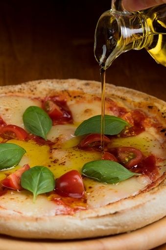 Olivenöl wird aus einer Flasche über eine Pizza mit Basilikum geträufelt
