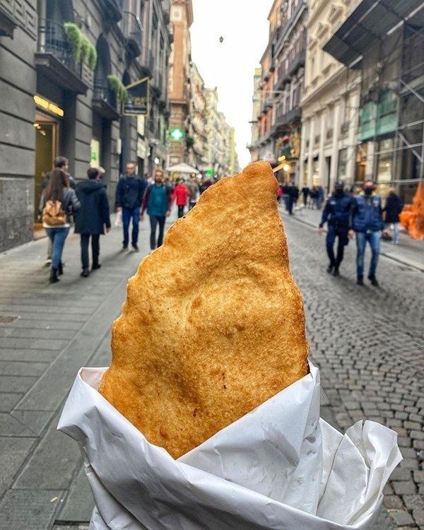 Goldbraune Pizza fritta in Papier vor einer belebten Altstadtstraße