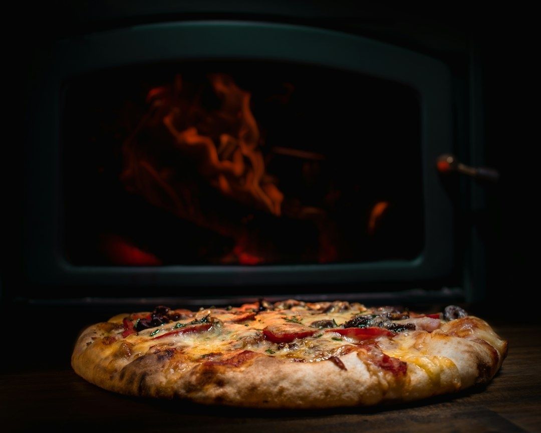 Pizza mit gebräuntem Rand vor einem glühenden Ofenfeuer
