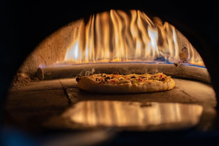 Pizza mit Belag auf einem Pizzastein im heißen Ofen