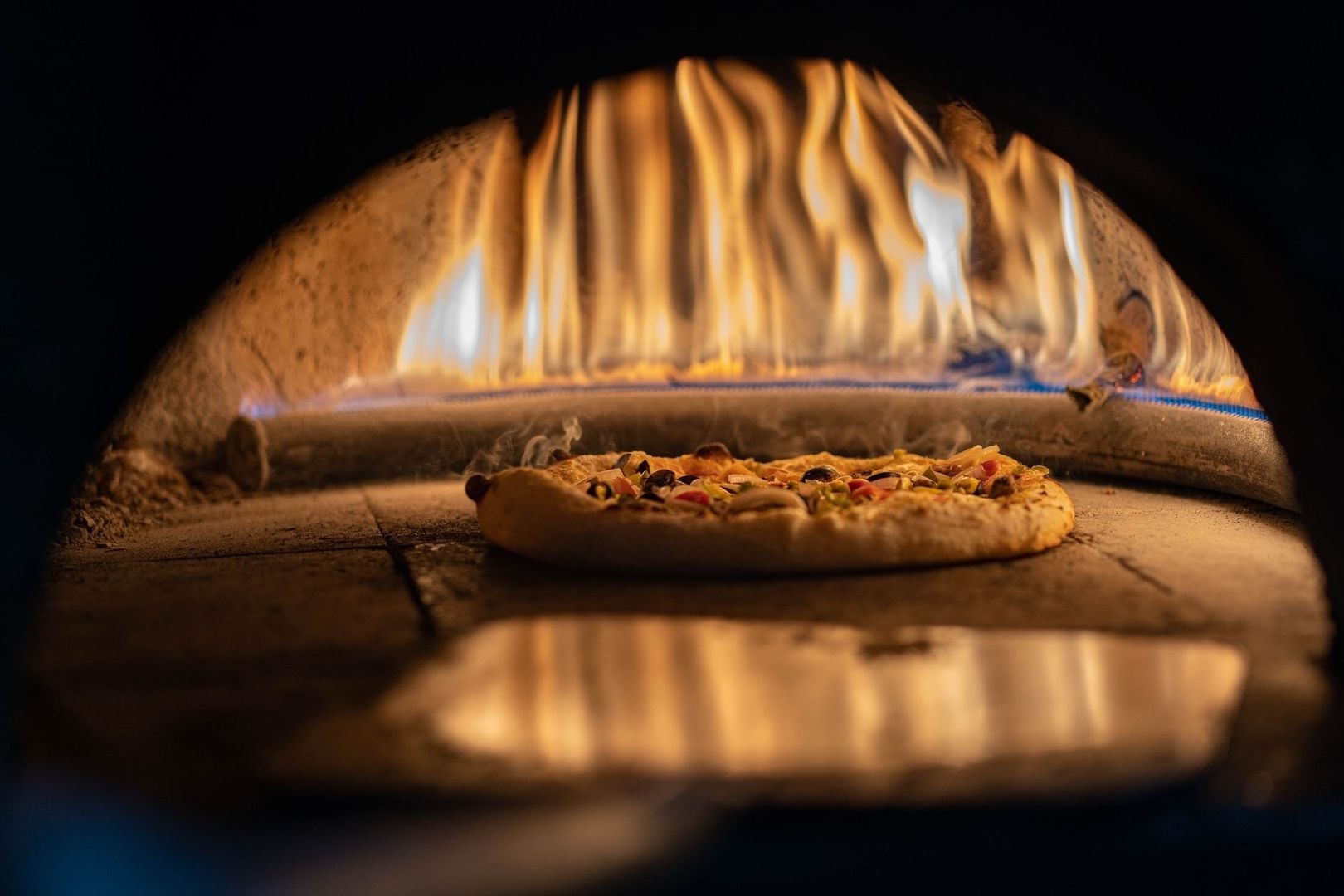 Pizza mit Belag auf einem Pizzastein im heißen Ofen